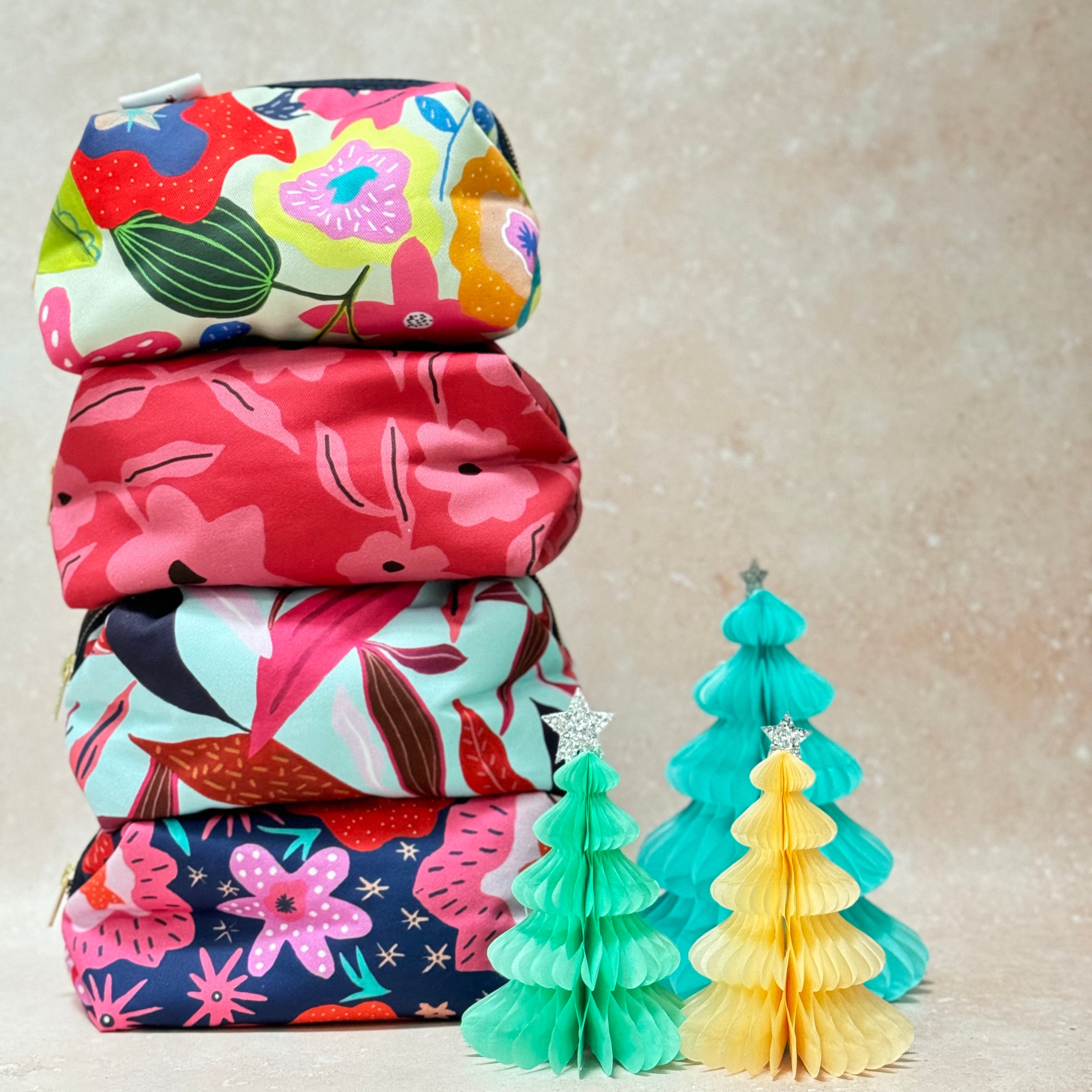 Stack of colourful large makeup bags by Jennie Fynn next to paper Christmas decorations
