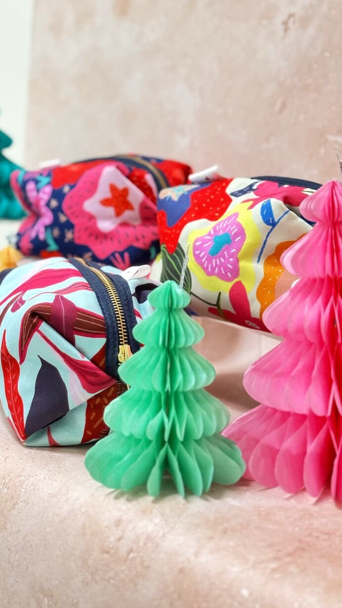 Colourful patterned large makeup bags made in the UK next to small paper Christmas trees