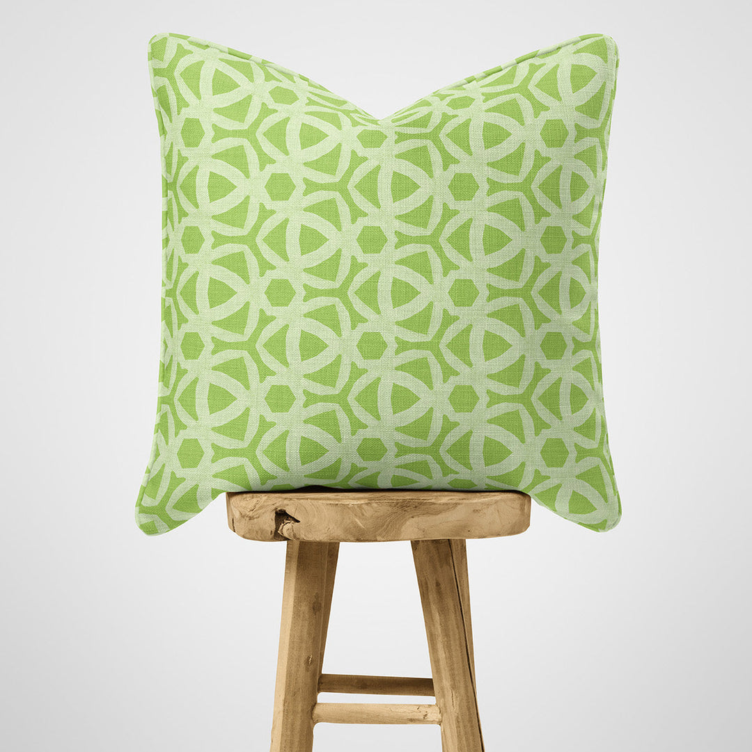 Green patterned pillow on a wooden stool against a white background