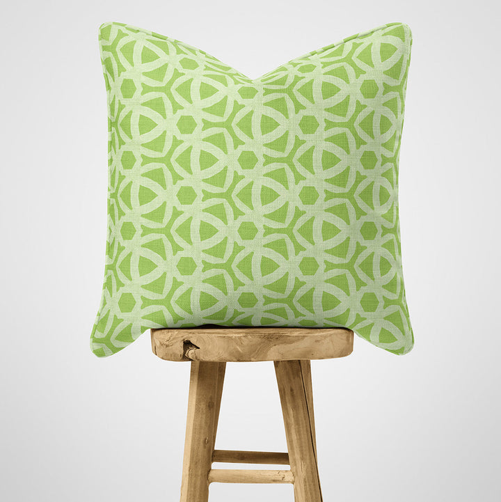 Green patterned pillow on a wooden stool against a white background