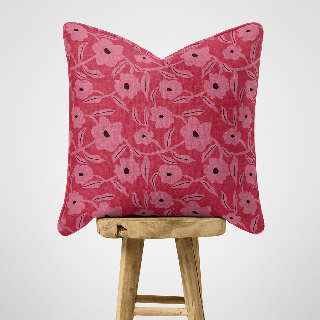 Pink floral cushion on a wooden stool against a white background