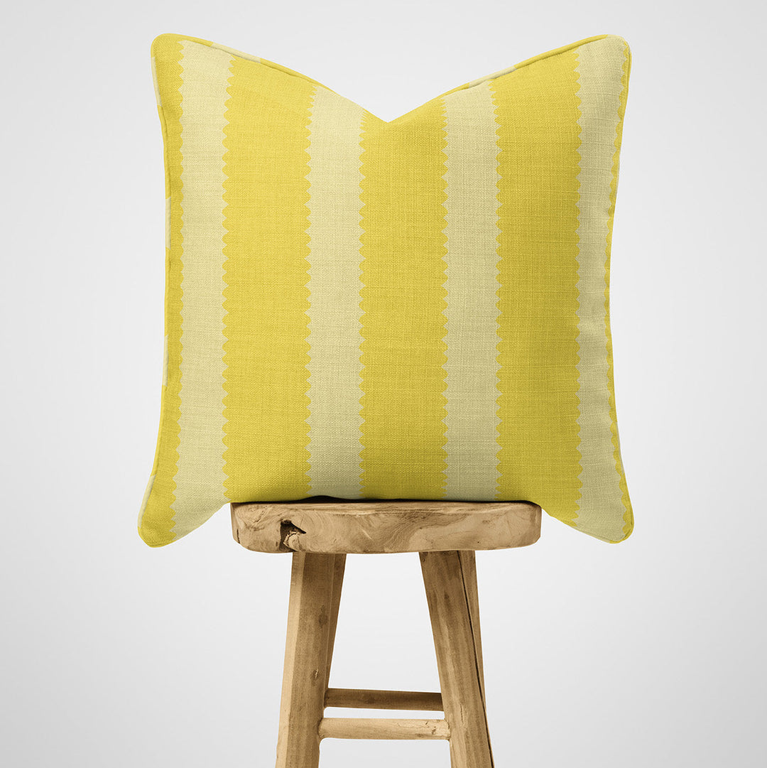 Yellow  scallop striped cushion on a wooden stool against a light gray background