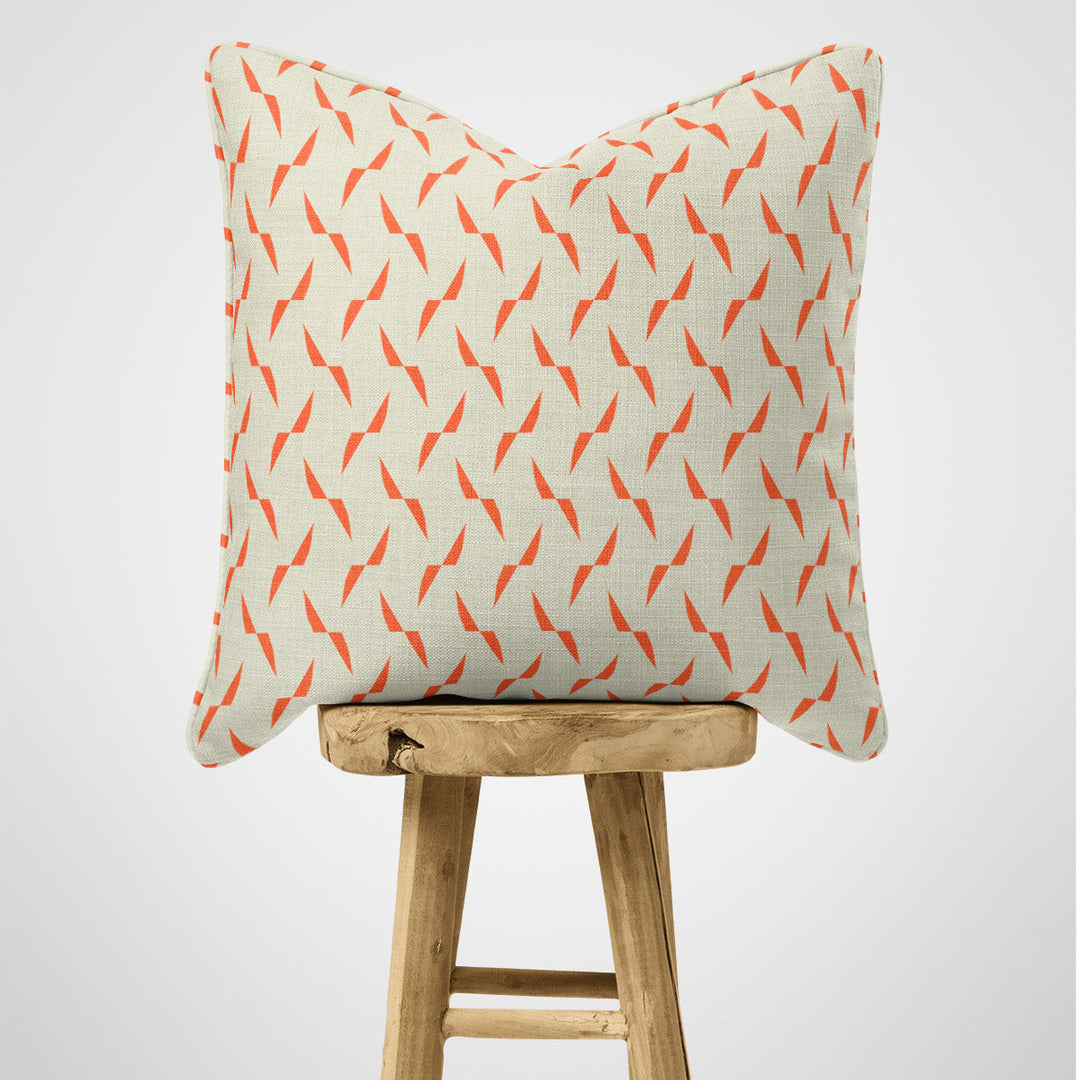 Organic Cotton Cushion in orange geometric pattern on a wooden stool against a light grey background