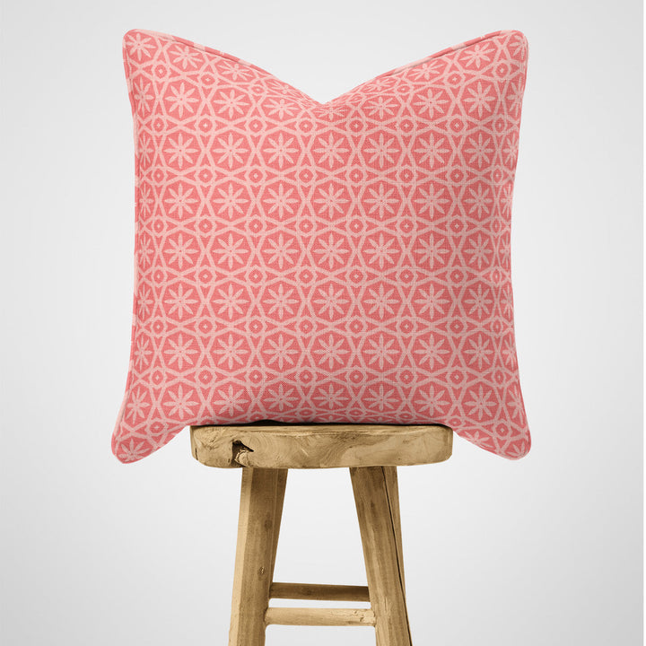 Pink geometric patterned cushion on a wooden stool against a light grey background